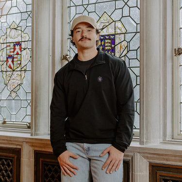 Male model wearing the black Sigma Alpha Epsilon Embroidered Luxe Quarter Zip in front of stained glass windows with fraternity crests.