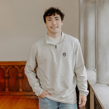 Male model wearing the smoke-colored Sigma Alpha Epsilon Embroidered Luxe Quarter Zip with crest embroidery, standing by a window in a formal setting.