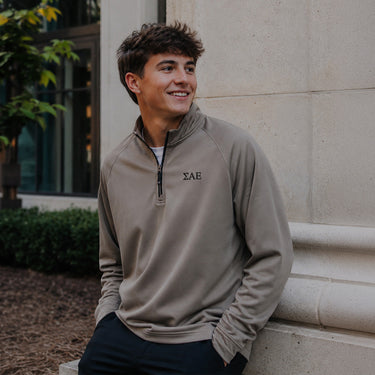 College-aged man wearing the Mushroom Cutter & Buck Adapt quarter-zip with black embroidered Sigma Alpha Epsilon Greek letters outdoors on campus.