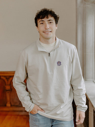 Male model wearing the smoke-colored Sigma Alpha Epsilon Embroidered Luxe Quarter Zip with crest embroidery, standing by a window in a formal setting.