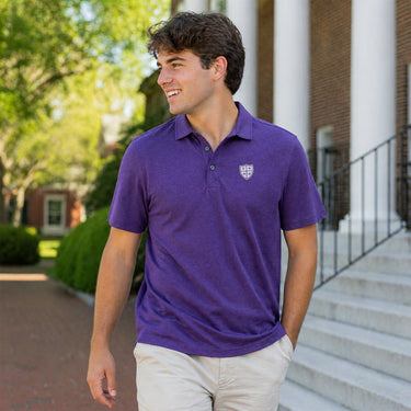 Man wearing a purple Cutter & Buck polo with a small shield crest on the chest, walking outdoors on a college campus.