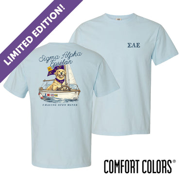 Light blue Comfort Colors t-shirt shown front and back; front features small Greek letters on the left chest, back displays a golden retriever sailing a boat with script text above and “Chasing Open Water” below.